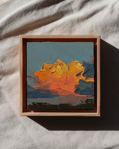 an abstract painting in a wooden frame on a white cloth covered surface with sunlight coming through the clouds