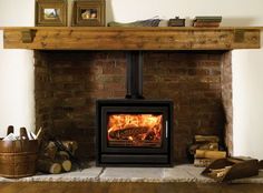 a wood burning stove in a brick fireplace with logs and firewood around it on the floor