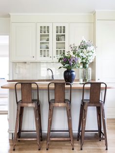 the kitchen has three stools in front of the island with two vases on it