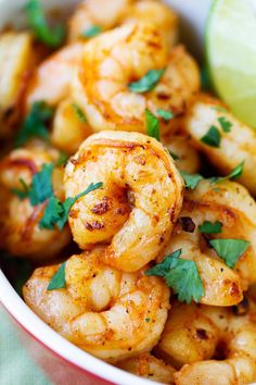 a bowl filled with cooked shrimp and garnished with cilantro, parsley and lime