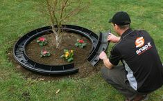 a man kneeling down in front of a small tree with flowers growing out of it