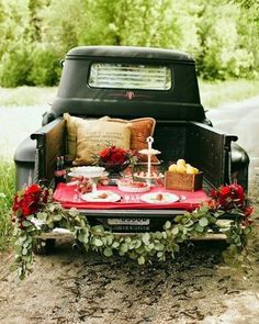 an old pickup truck is decorated with red flowers and greenery for a festive picnic