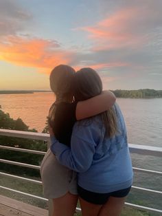 two girls hugging each other on a balcony overlooking the water at sunset or sunrise with their arms around each other