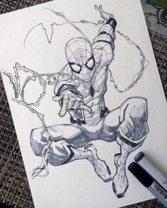 a drawing of spider - man on paper next to a pen and inking tool