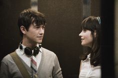 a young man and woman standing next to each other in front of a wall with headphones on