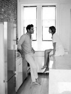 the man and woman are sitting on the counter in the kitchen looking at each other