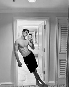 a shirtless man taking a selfie in front of an open door with his cell phone