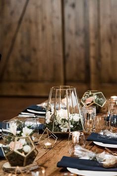 a wooden table topped with lots of plates and vases filled with white flowers next to candles