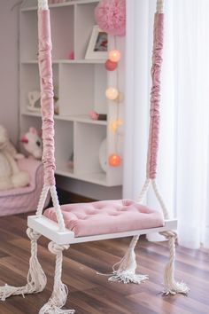 a pink hanging chair with tassels on the bottom and sides, in front of a white bookcase