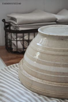 a large white vase sitting on top of a striped table cloth next to a basket