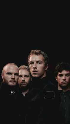 five men are standing in front of a black background and one is looking at the camera