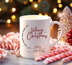 a white coffee mug with merry christmas written on it next to some candy canes