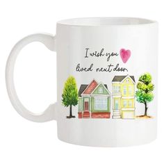 a white coffee mug with houses and trees on the front, which says i wish you lived next door