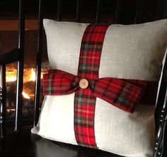 a red and black plaid pillow with a wooden button on the side sitting in front of a fire place