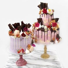 two cakes decorated with chocolate, strawberries and flowers on top of a marble table