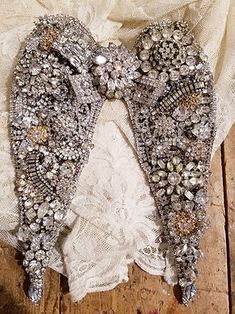 an angel wings on top of a white lace covered table cloth with beads and pearls