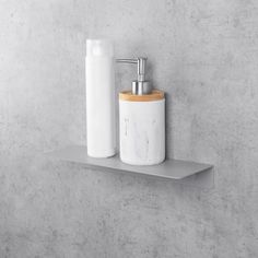 a white toilet brush and soap dispenser on a gray shelf against a concrete wall