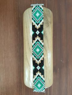 a beaded bracelet on a wooden surface with a metal clasp in the center and green, white, and black beads