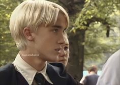 a young man with blonde hair wearing a suit and tie looking off to the side