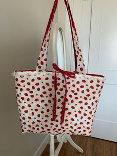 A handbag with a beige strawberry print on the outside and a beige lace material at the top, around the edge of the bag. It has a red polka dot material on the inside with two red polka dot strings. The two strings can be turned into a bow for a cute way to close the bag. Cute Fabric Bags For Gifts, Rectangular Bags With Strawberry Print As Gift, Rectangular Strawberry Print Bag As A Gift, Rectangular Bags With Strawberry Print For Gifts, Rectangular Bag With Strawberry Print As Gift, Red Bag With Strawberry Print As Gift, Rectangular Strawberry Print Bag For Gifts, Strawberry Elephant, Trendy Pink Bag With Strawberry Print