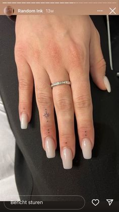 a woman's hand with white nails and a cross tattoo on her ring finger