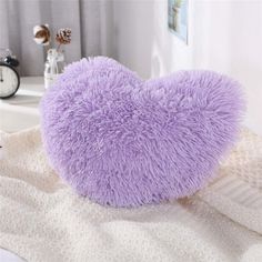 a purple heart shaped pillow sitting on top of a white bed next to a window