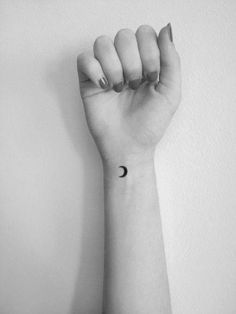 a woman's arm with a small black moon tattoo on the left side of her wrist