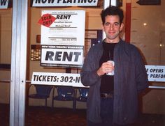 a man standing in front of a rental store holding a drink and looking at the camera