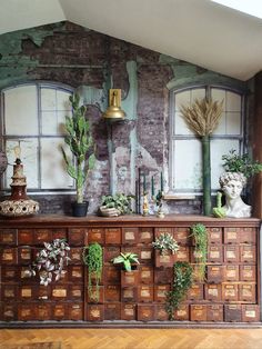 an old dresser is decorated with plants and other decor items in front of a brick wall