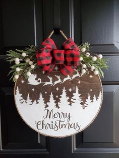 a wooden sign that says merry christmas hanging on a door with red and black plaid bow