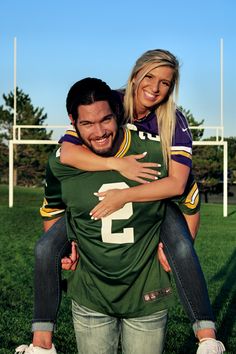 a man holding a woman on his back in the grass with a football field behind him