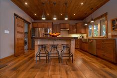 a kitchen with wood flooring and wooden cabinets in the center, along with two bar stools