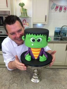 a man holding up a cake with a green monster face on it's head