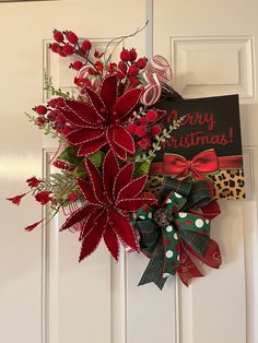 a red and green christmas wreath hanging on a door with a merry christmas sign in the background