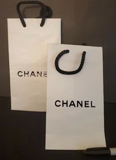 two bags with the word chanel written on them are sitting next to a pen