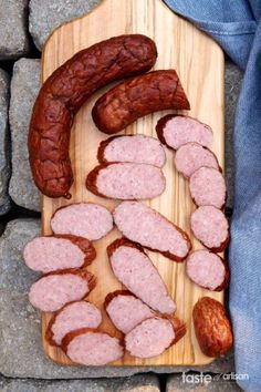 some sausages are on a wooden cutting board next to rocks and a blue towel