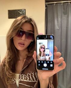 a woman taking a selfie with her cell phone in front of her face and wearing sunglasses