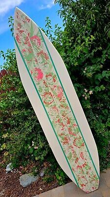 a white surfboard sitting on top of a sidewalk next to some bushes and trees