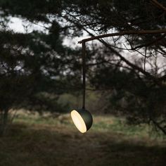 an outdoor light hanging from a tree in the woods at dusk or dawn with no one around it