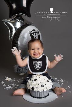 a baby sitting in front of a black and silver cupcake