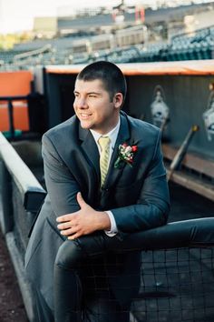 a man in a suit and tie leaning on a fence with his arms crossed, looking off into the distance