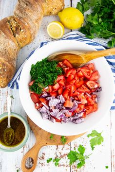 a white bowl filled with tomatoes, onions and parsley next to a loaf of bread