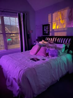 a bed in a room with purple lighting on the walls and pillows, along with a laptop