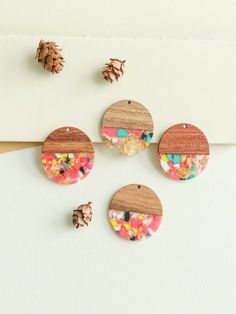 three wooden buttons with confetti and sprinkles on them next to pine cones