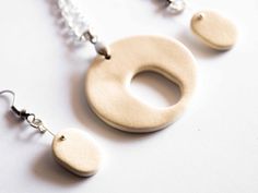 two wooden pendants are hanging from chains on a white surface, one is shaped like a circle and the other has a chain attached toggle