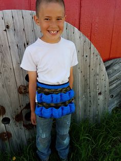 a young boy standing in front of a wooden fence wearing a blue and black skirt