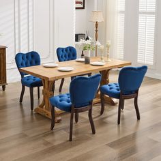 a dining room table with blue chairs and plates on the wooden table in front of it