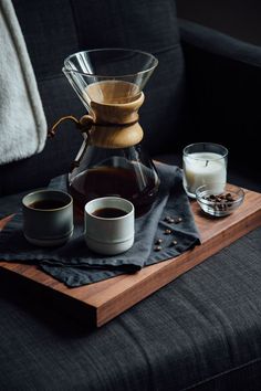 a coffee pot and two cups sit on a wooden tray next to a black couch