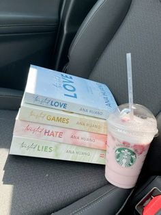 a stack of books sitting on top of a car seat next to a drink cup