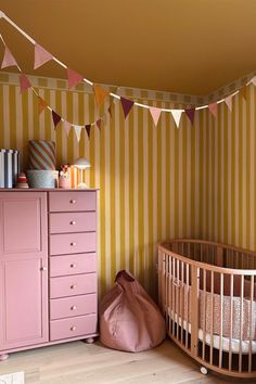 a baby's room with pink furniture and striped wallpaper, including a crib